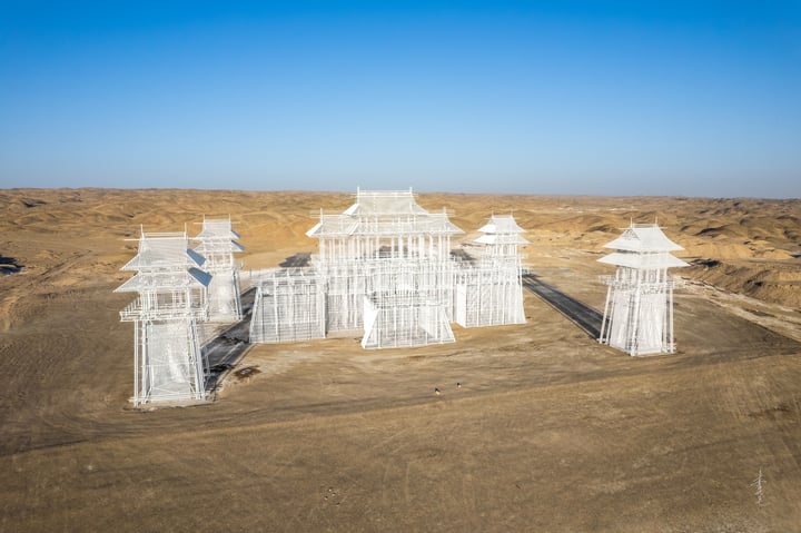 An aerial view of a white, pagoda-like structure with multiple levels and a central roof, surrounded by a barren desert landscape.