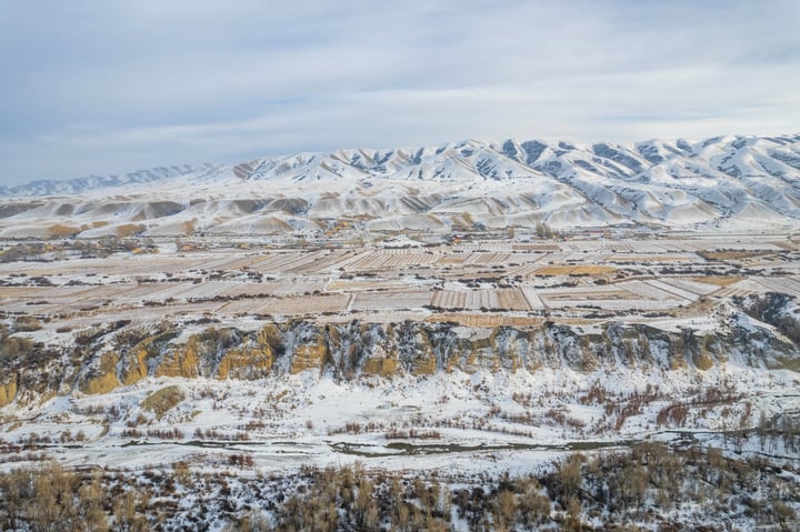 A snowy mountain range with a town in the valley, surrounded by a clear blue sky.