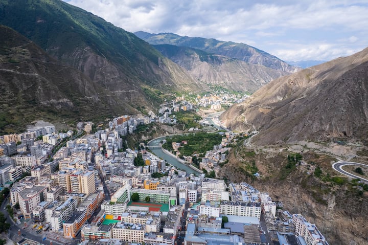 An aerial view of a city nestled in a valley, surrounded by mountains and a winding river, with buildings of varying heights and colors.